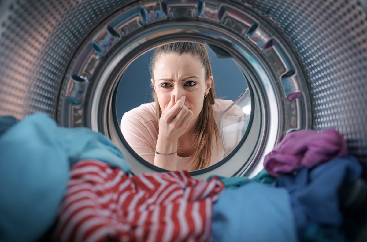 Woman staring at the laundry in the washing machine and holding her nose