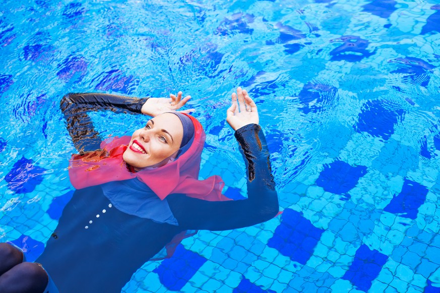 muslim woman in red hijab swimming in a pool (lying on a back)