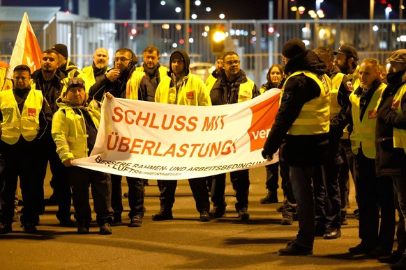 26.02.2023, Nordrhein-Westfalen, Köln: Streikende in Warnkleidung halten ein Banner der Gewerkschaft Verdi mit der Aufschrift: «Schluss mit Überlastung!». Airport-Mitarbeiter der Luftsicherheit des Fl ...