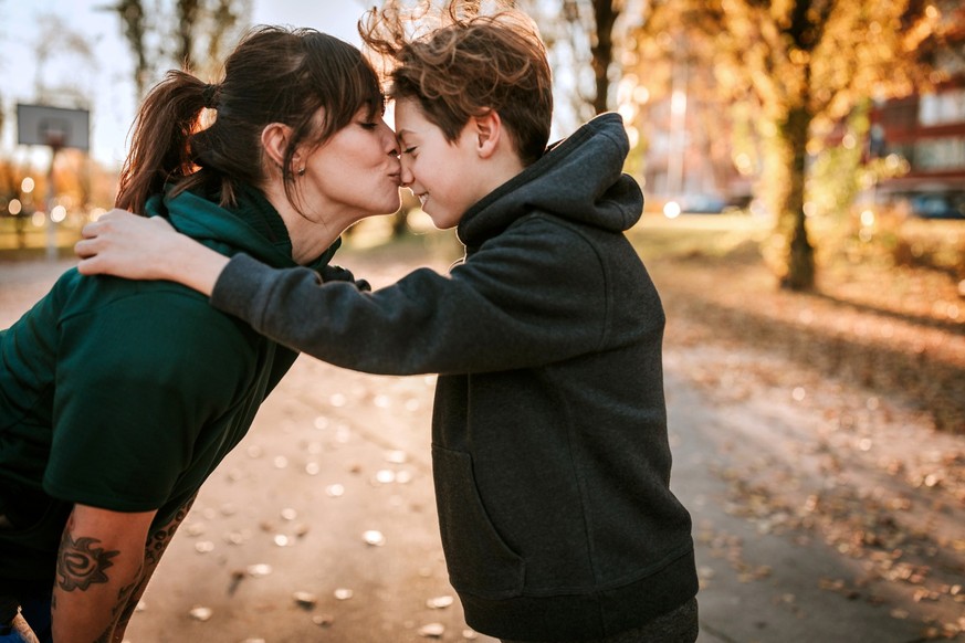 Young woman kissing and embracing her son outdoor, standing face to face on sunny day