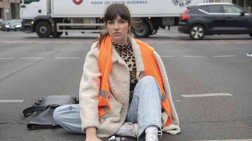 16.05.2023, Berlin: Carla Hinrichs, Sprecherin der Klimagruppe Letzte Generation, sitzt bei einer Straßenblockade der Letzten Generation mit einer auf den Asphalt festgeklebten Hand auf der Straße. Fo ...