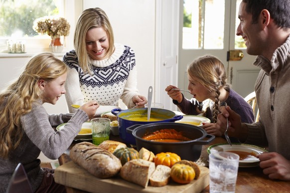 Junge Familie am herbstlich gedeckten Essenstisch beim Essen einer Suppe