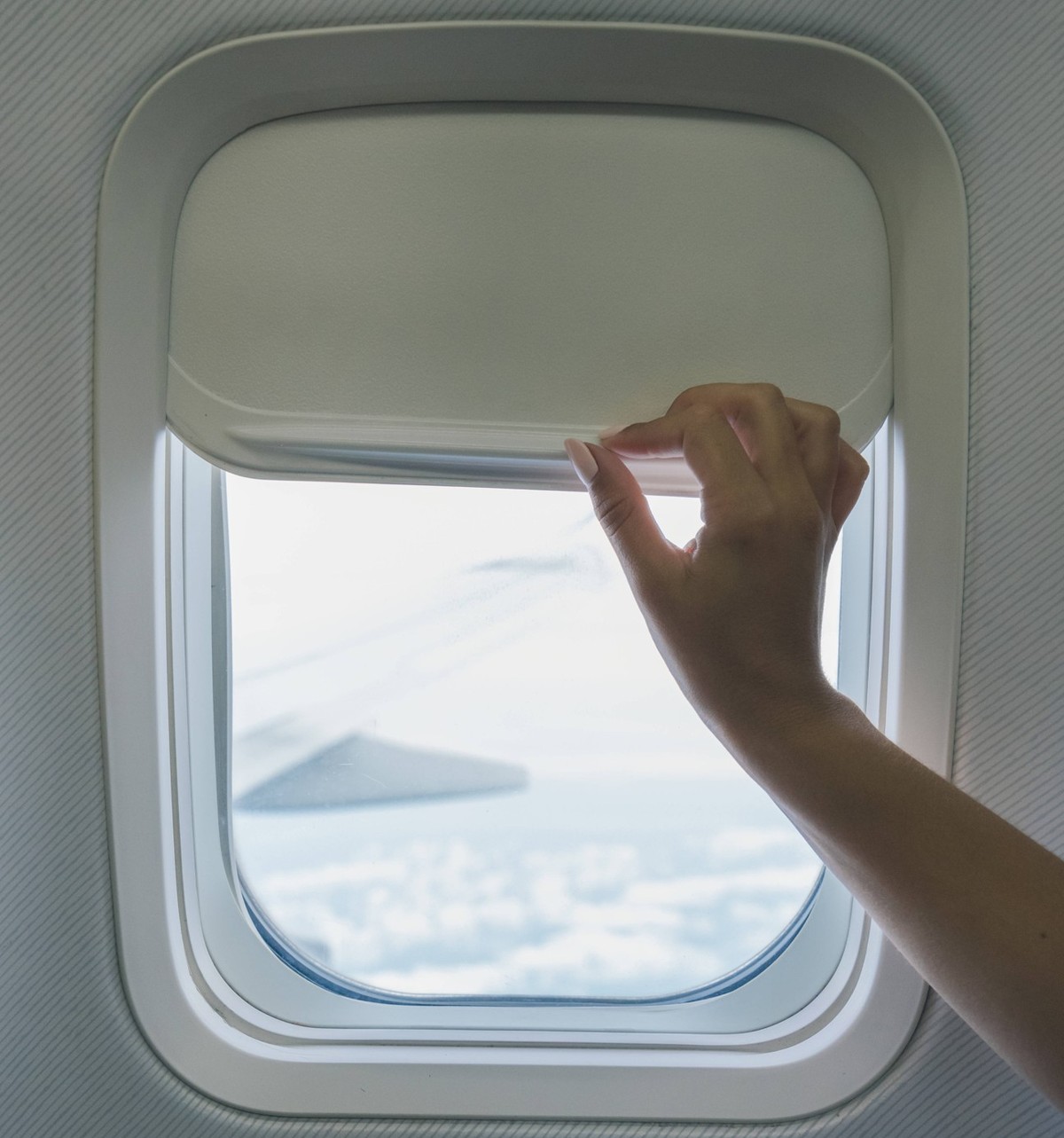 Unrecognizable passenger opening blind in aircraft Crop traveler opening shadow on window in airplane with clouds seen through window in sunshine during flight EricPanades_ID15014_458551_005 Copyright ...