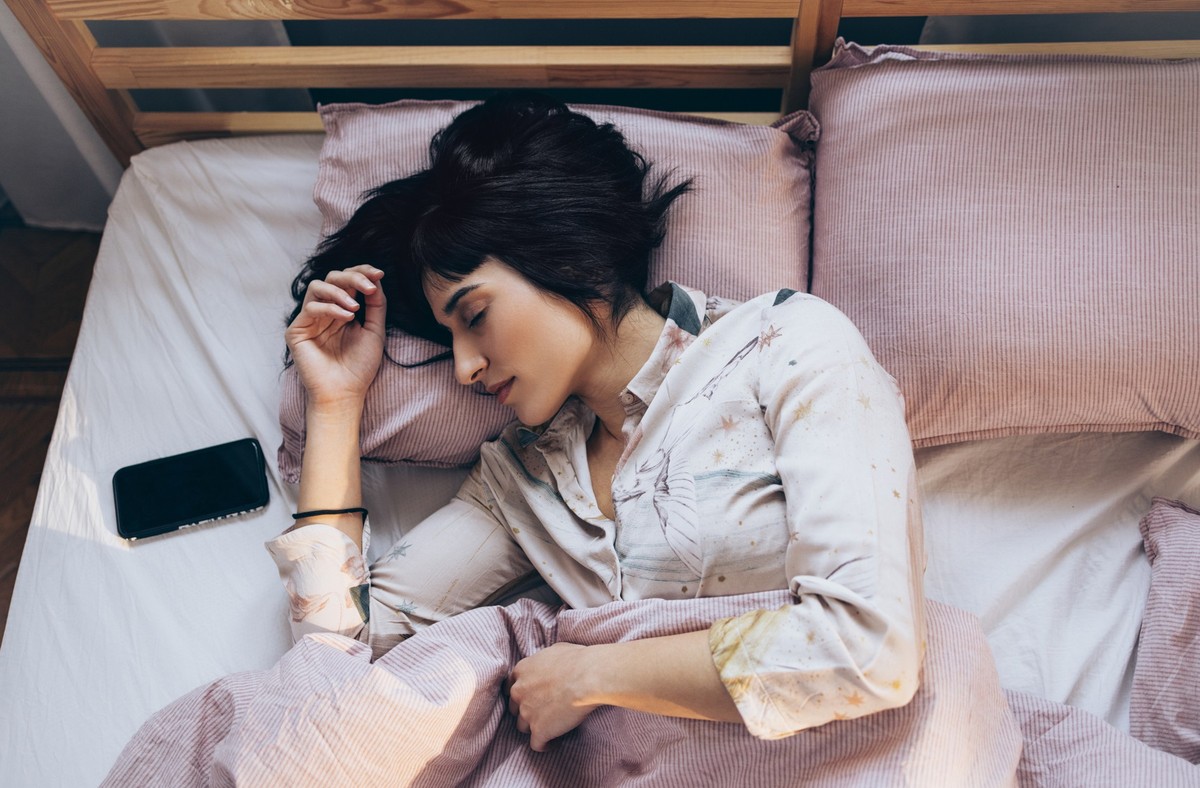 An overhead view of a woman listening to music on her smartphone while sleeping.