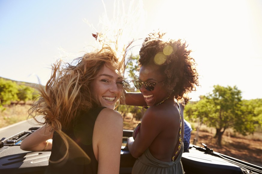 Two women standing in the back of open car turning to camera