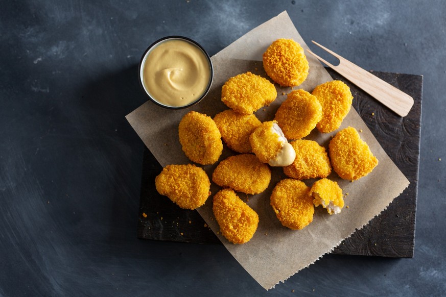 Tasty appetizing crispy chicken nuggets served on wooden board with mustard on dark background.