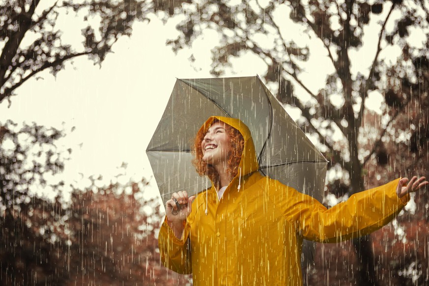 Happy young woman in yellow raincoat having fun on a rainy day in nature