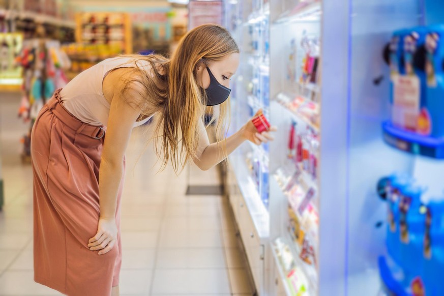 Alarmed female wears medical mask against coronavirus while purchase of household chemicals in supermarket or store- health, safety and pandemic concept - young woman wearing protective mask and stock ...