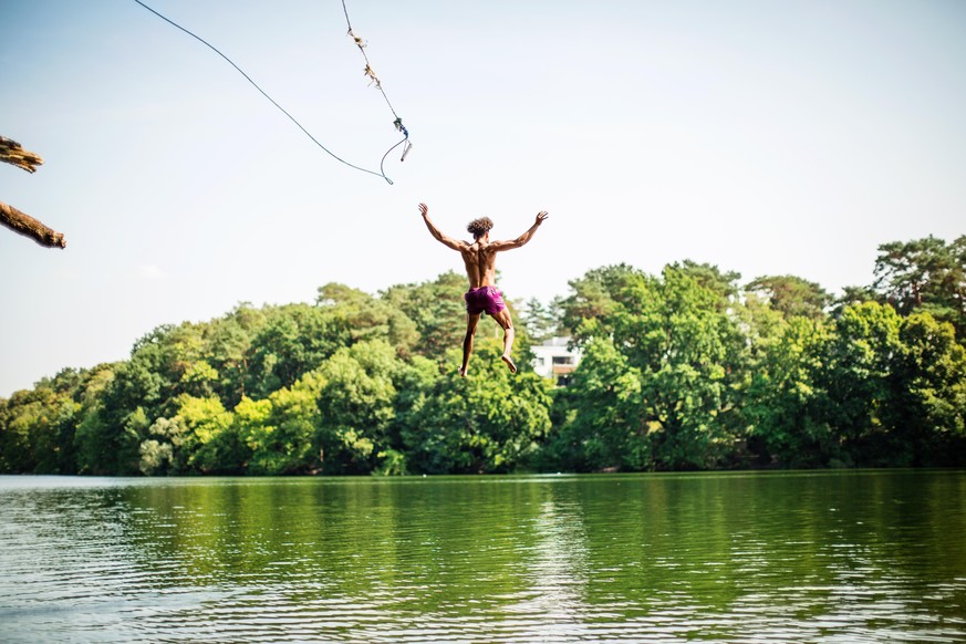 Young man jumping into the lake from the swinging rope. Man jumping into the lake water with a rope.