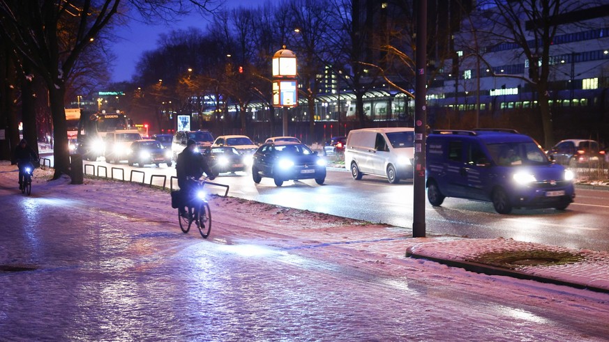 17.01.2024, Hamburg: Radfahrer sind auf einem vereisten Radweg neben einer Hauptverkehrsstra