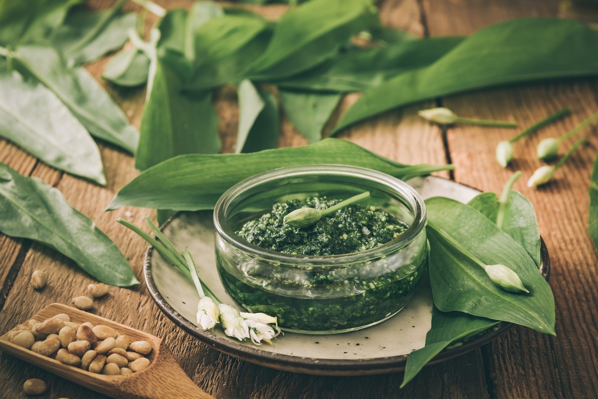 Homemade wild garlic pesto in a glass bowl on wooden background, decorated with leaves and pine nuts, desaturated colors