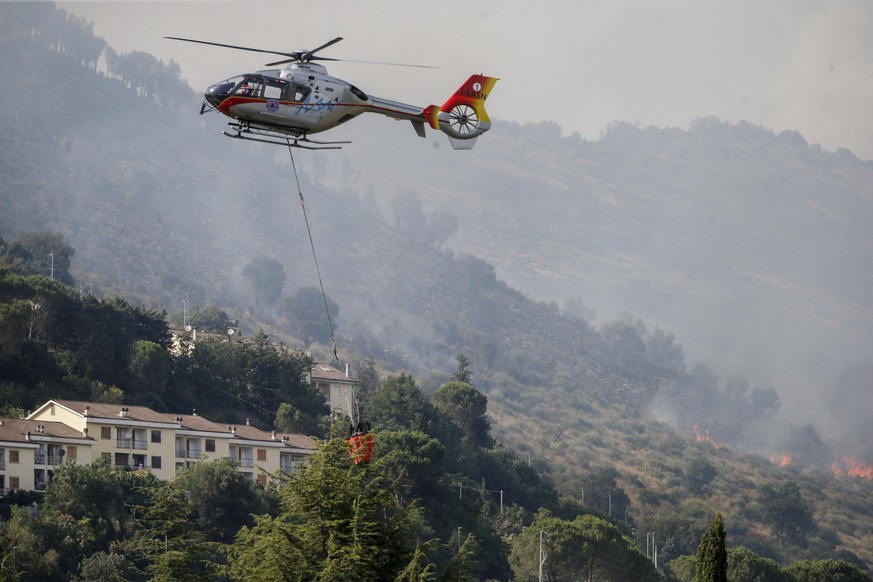 Rauch steigt von einem Feuer im Bergpark Catillo in der Nähe von Tivoli, auf, während ein Löschhubschrauber darüber Wasser abwirft.
