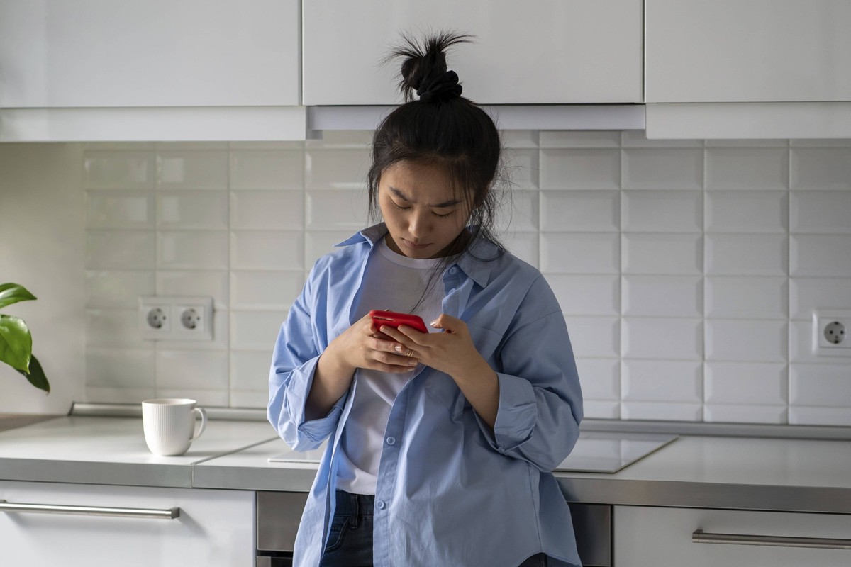 Stirnrunzelnd verärgert asiatische junge Frau hält Smartphone erhalten Nachricht oder E Mail mit schlechten Informationen. Upset verwirrt chinesische Mädchen sieht auf Handy sehen wichtigen Anruf verp ...