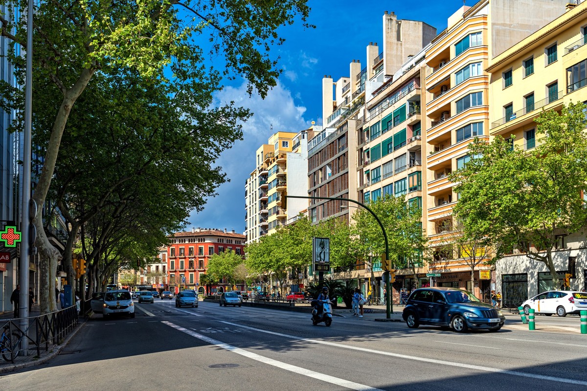 PALMA, SPAIN - APRIL 12, 2019: Urban road, green trees and modern buildings under blue sky in Palma - capital and largest city of Balearic islands, famous resort and tourist destination.