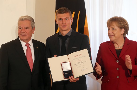 Fußball-Nationalspieler Toni Kroos (M) präsentiert das Silberne Lorbeerblatt neben Bundespräsident Joachim Gauck (l), Bundeskanzlerin Angela Merkel (CDU) am 10.11.2014 im Schloss Bellevue in Berlin. D ...