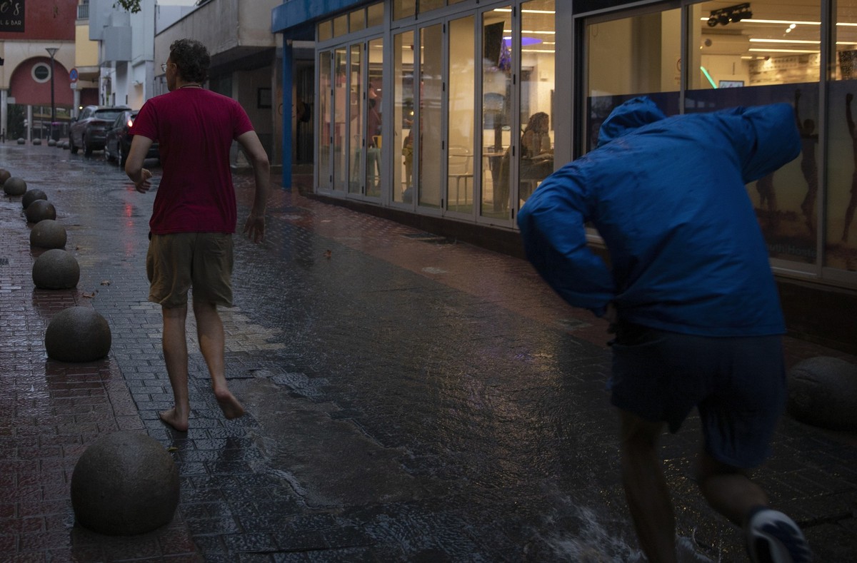 01.11.2024, Spanien, Palma: Menschen laufen während eines Regenschauers in Palma über die Straße. Auch die Balearen erwarten Unwetter auf den beliebten Touristeninseln Mallorca und Menorca. Bisher gil ...