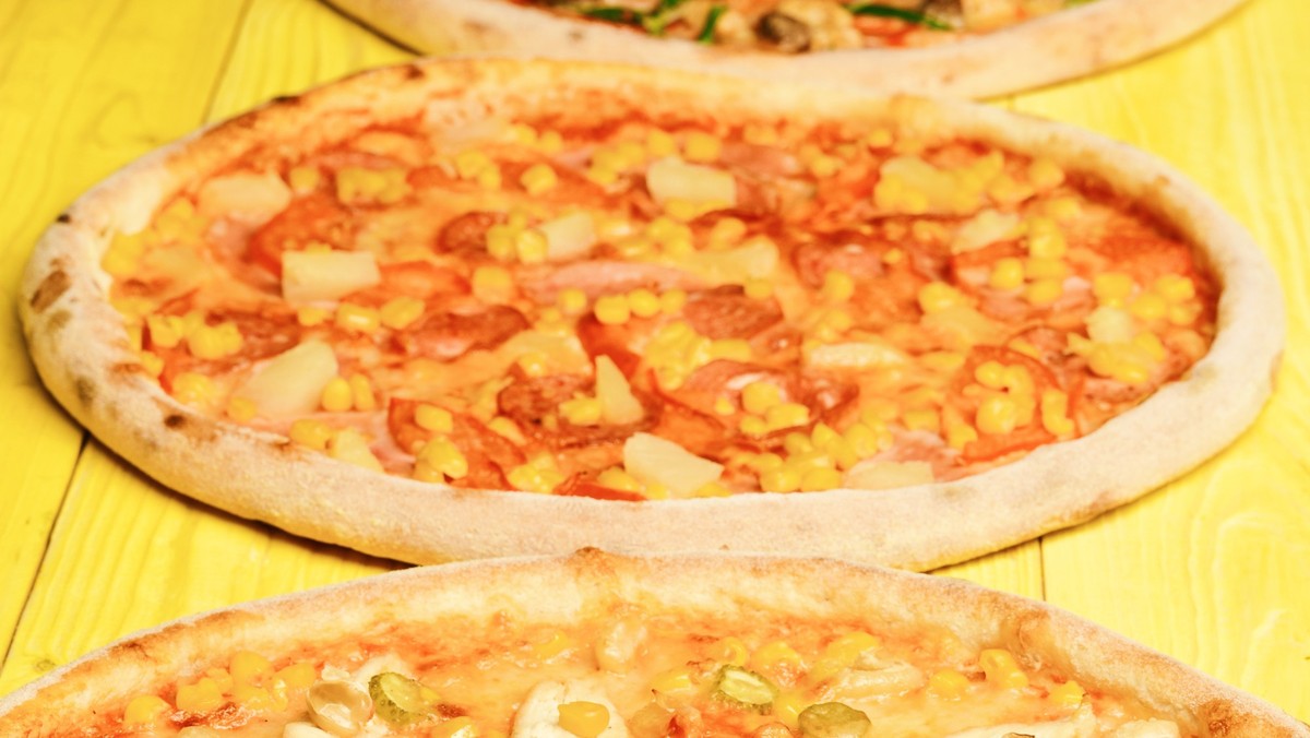Italian pizza and pizzeria concept. Hawaii pizza with meat, corn, tomatoes and cheese on yellow wood background. Take away food with various ingredients and crunchy edges. Different pizza set for menu ...