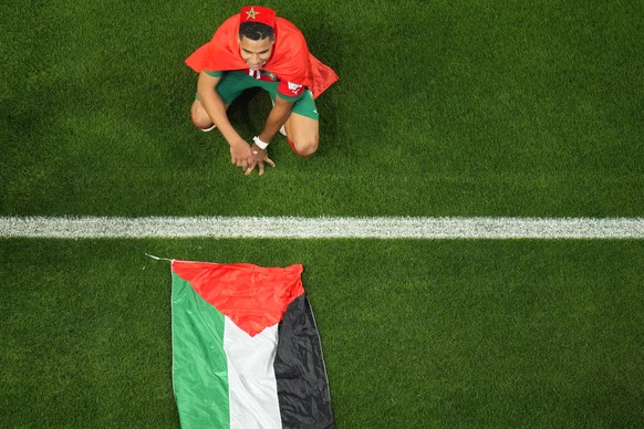 Morocco's Abdelhamid Sabiri celebrates, sitting by the Palestinian flag, after the World Cup round of 16 soccer match between Morocco and Spain, at the Education City Stadium in Al Rayyan, Qatar, Tues ...