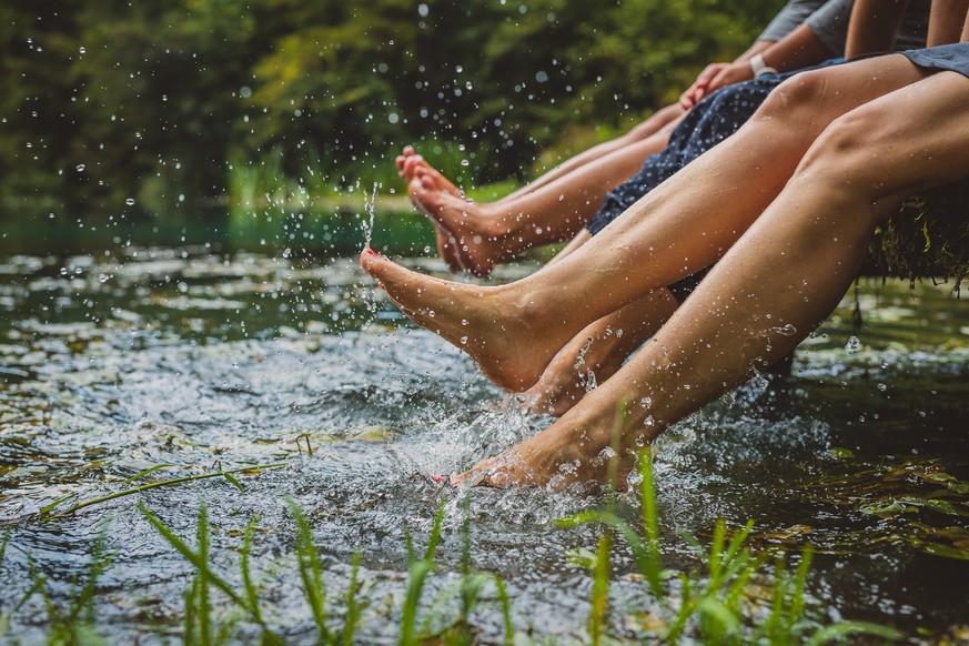 Detail of three young women with nice nails relaxing on a wooden pier and splashing their feet into cold water. Picturesque clean lake with women splashing their feet in water