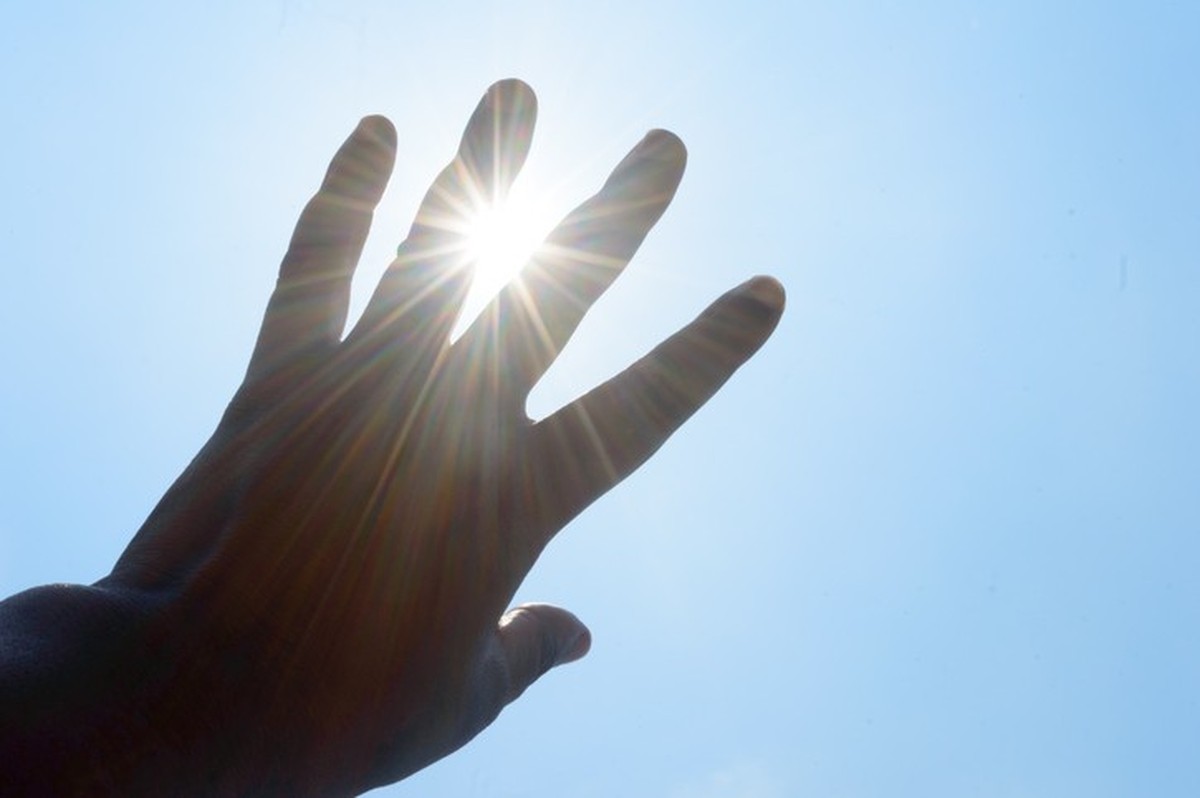 Hot summer sunlight rays pouring through human hand. Hand covering sun light heat temperature. Protection from ultraviolet light and sunburn background. Sunstroke, heatstroke, greenhouse effect.