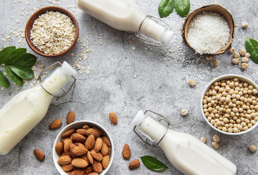 Alternative types of vegan milks in glass bottles on a concrete background. Top view