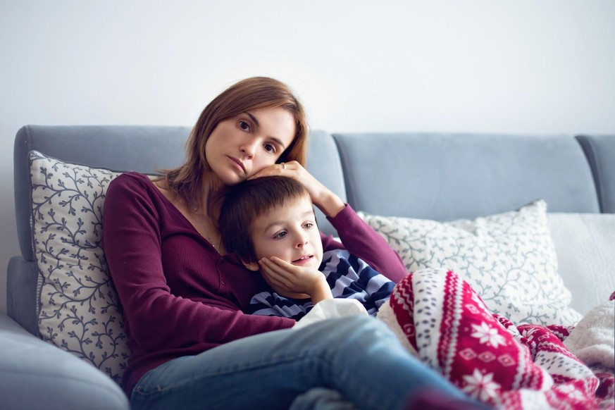 Young mother, holding her little sick boy, lying together on the couch