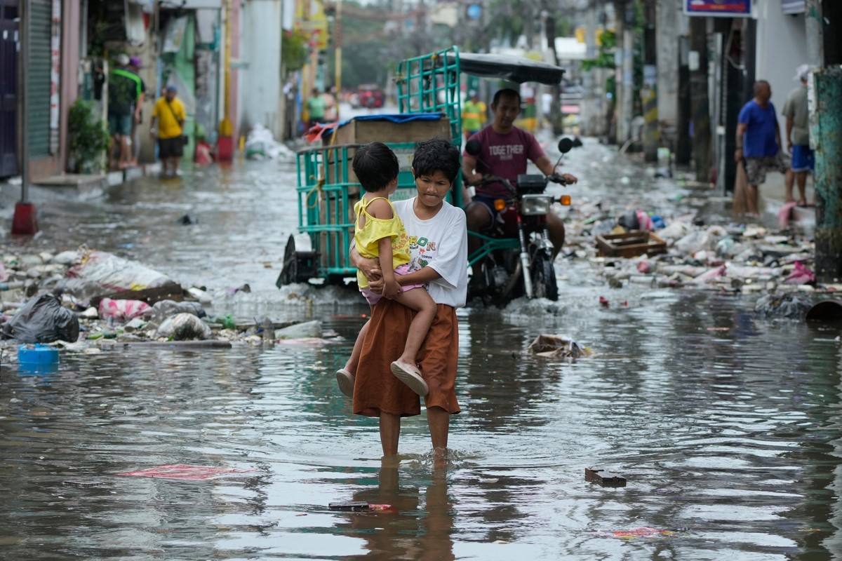 10.11.2025, Philippinen, Navotas: Eine Frau und ein Kind überqueren eine durch den Taifun «Fung-wong» überschwemmte Straße. Foto: Aaron Favila/AP/dpa +++ dpa-Bildfunk +++