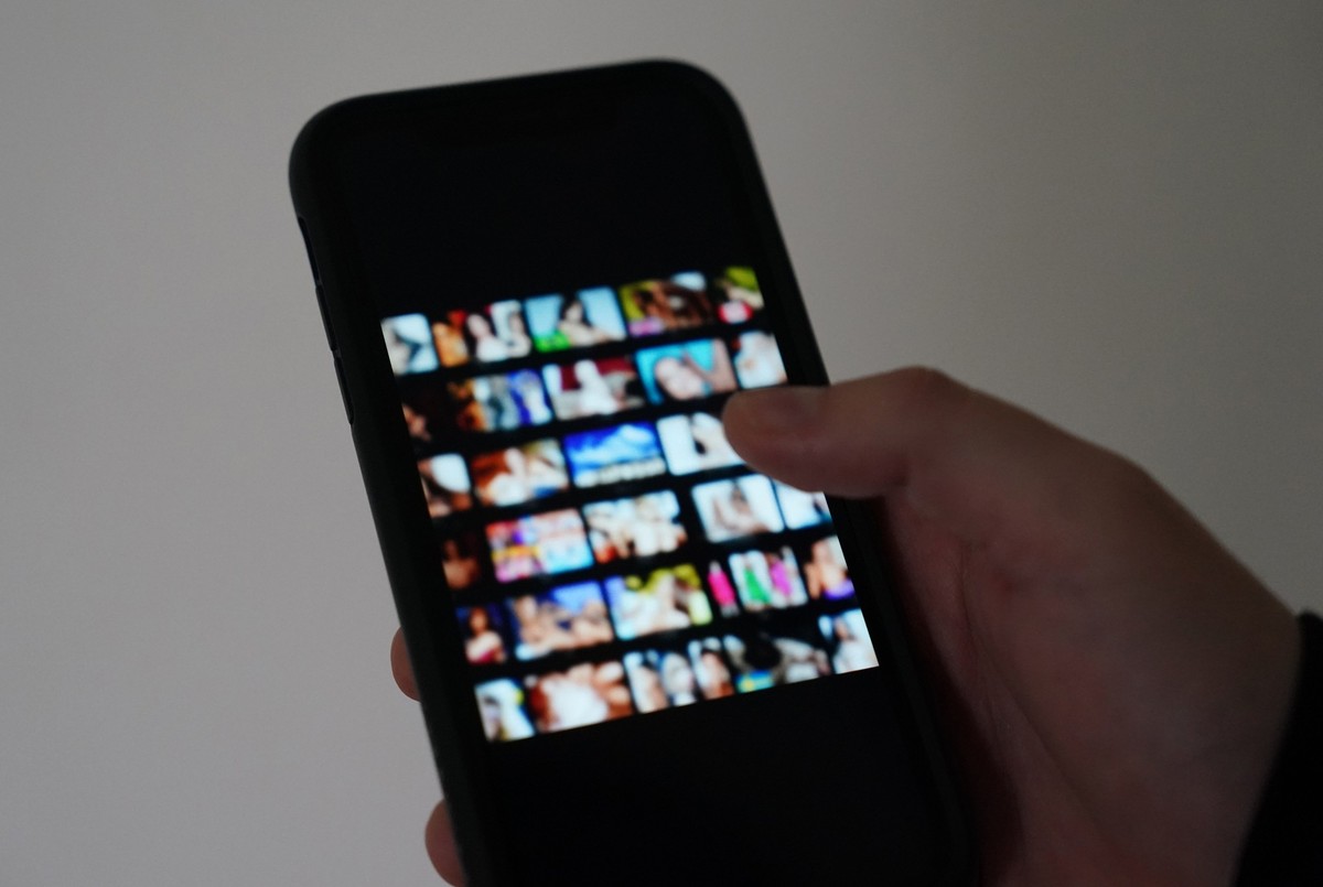 ILLUSTRATION - 19.10.2023, Hamburg: Ein Mann schaut sich auf einem Smartphone eine Porno-Internetseite an (gestellte Szene). Es beginnt mit einem vermeintlichen Online-Flirt und endet mit Geldforderun ...