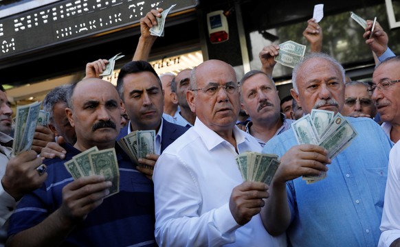 Businessmen holding U.S. dollars stand in front of a currency exchange office in response to the call of Turkish President Tayyip Erdogan on Turks to sell their dollar and euro savings to support the  ...