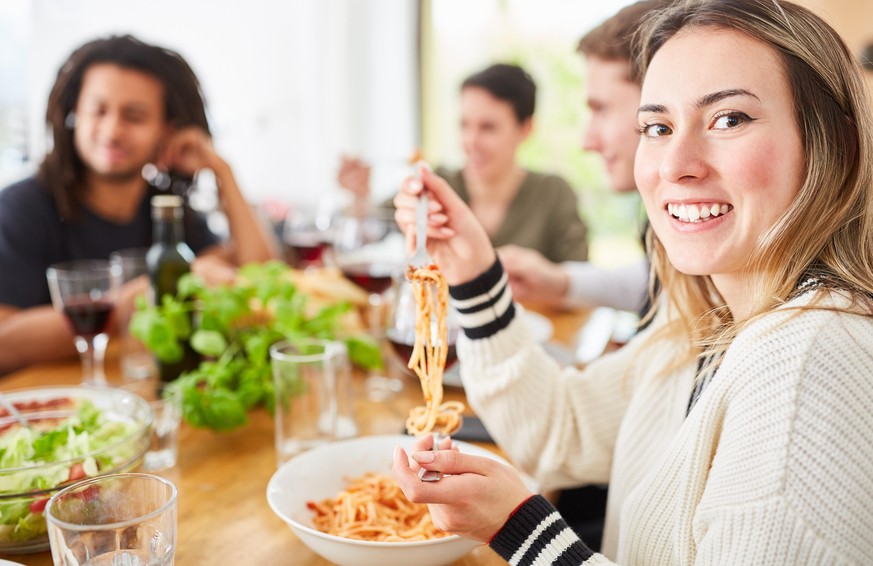 Freunde essen gemeinsam Spaghetti mit Tomatensauce in der Küche einer WG