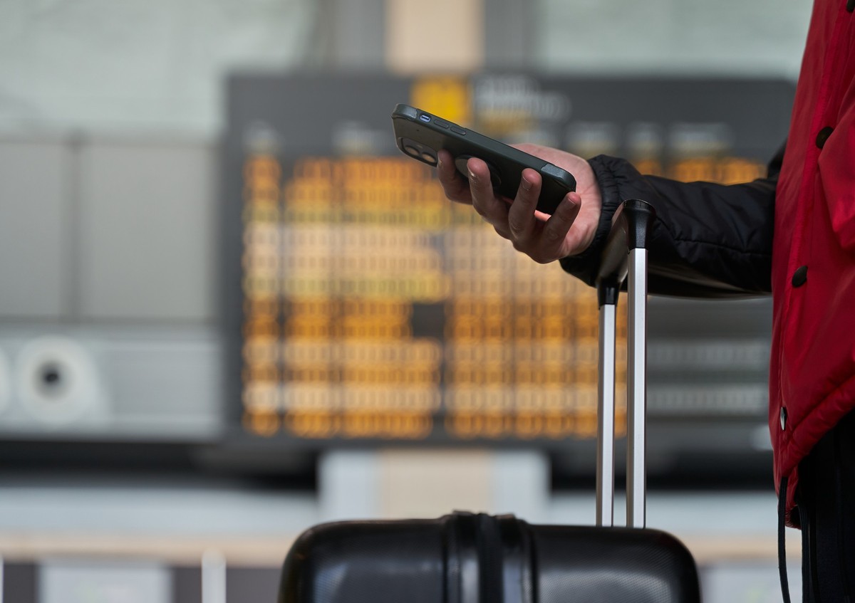 Detail of male hand checking phone by luggage and panel airport