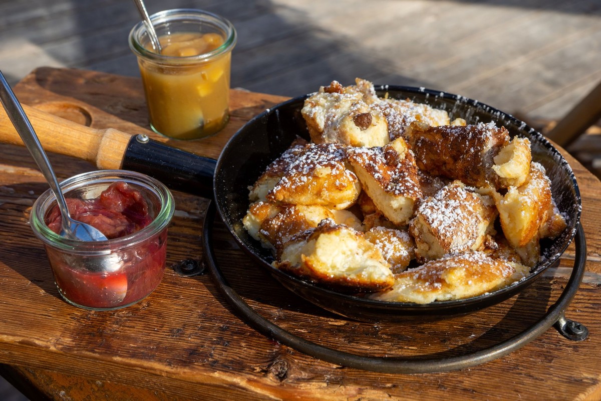 Traditioneller Wiener Kaiserschmarrn, zerkleinerte süße Pfannkuchen mit Rosinen, serviert in einer eisernen Pfanne auf alten Holzbrettern auf einem Schieferteller