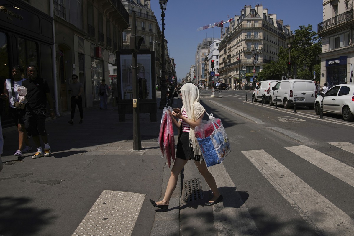 A woman protects her head during a heat wave, Monday, June 30, 2025 in Paris. (AP Photo/Christophe Ena)