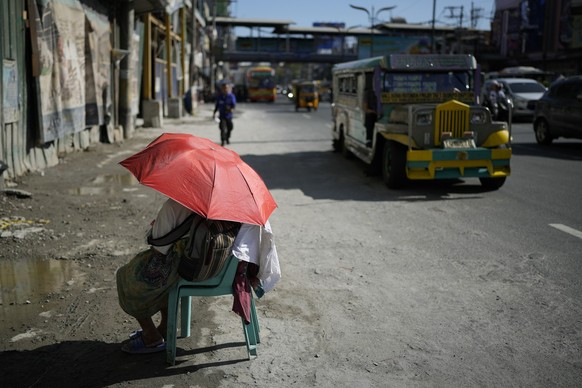 29.04.2024, Philippinen, Manila: Eine Straßenverkäuferin schützt sich mit einem Regenschirm vor der Sonne in einer Straße. Foto: Aaron Favila/AP/dpa +++ dpa-Bildfunk +++