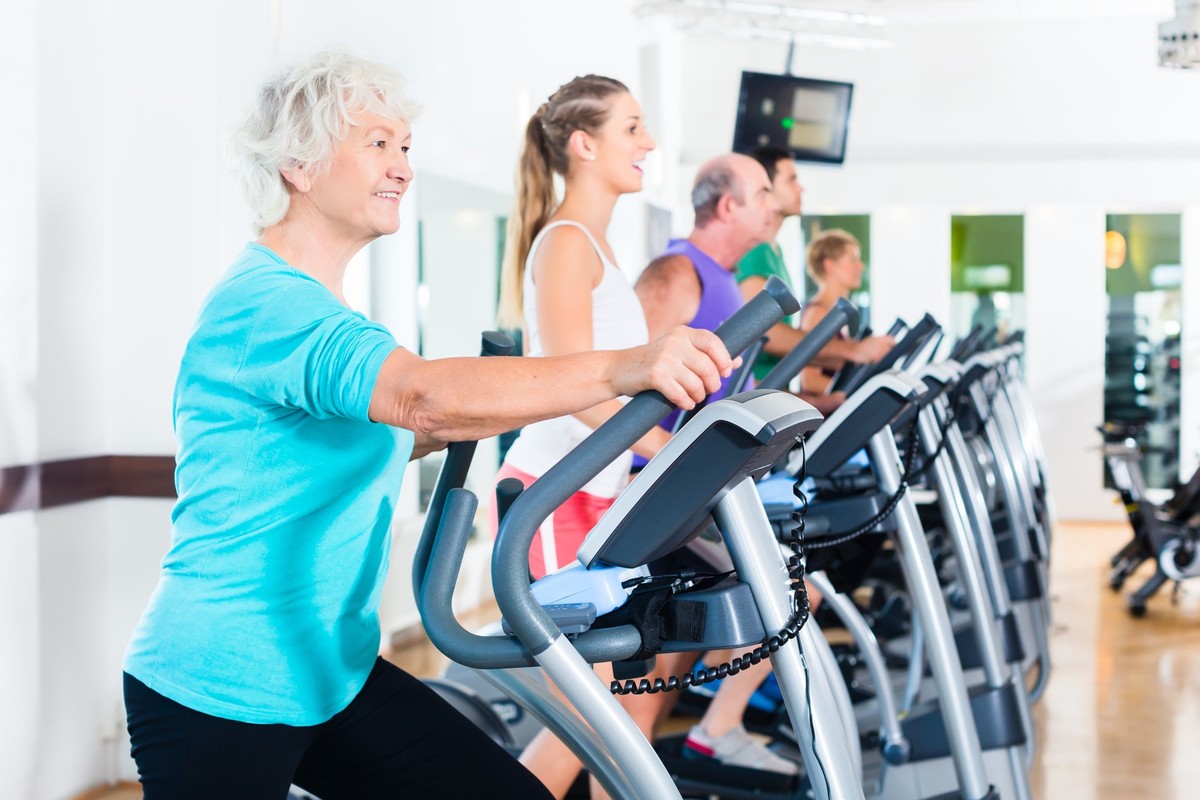 Group with young and Senior women and men on elliptical trainer exercising in gym