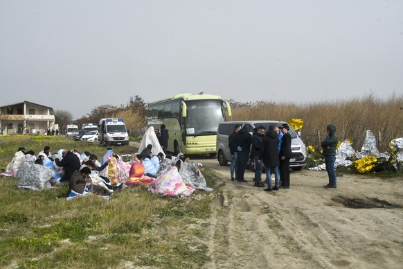 dpatopbilder - 26.02.2023, Italien, Cutro: Gerettete Migranten sitzen in Decken gehüllt an einem Strand in der Nähe von Cutro. Bei einem Bootsunglück mit Migranten an der süditalienischen Küste sind M ...