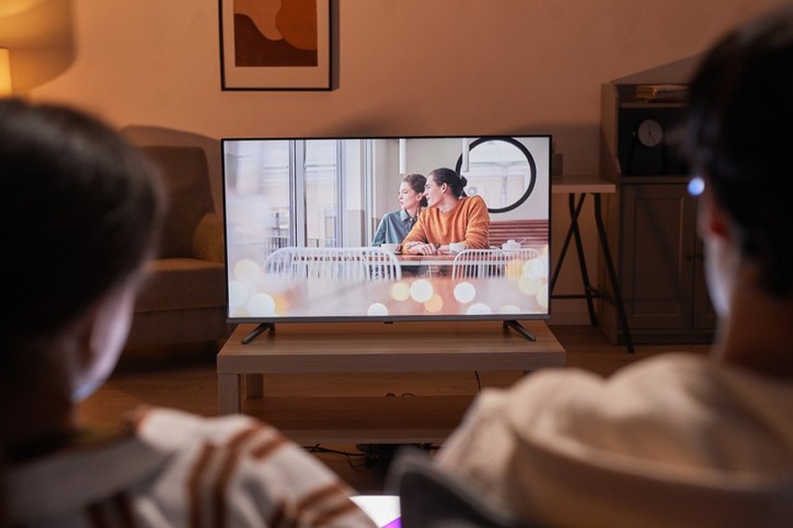 Back view of adult couple watching movies at home while sitting on sofa, focus on TV screen