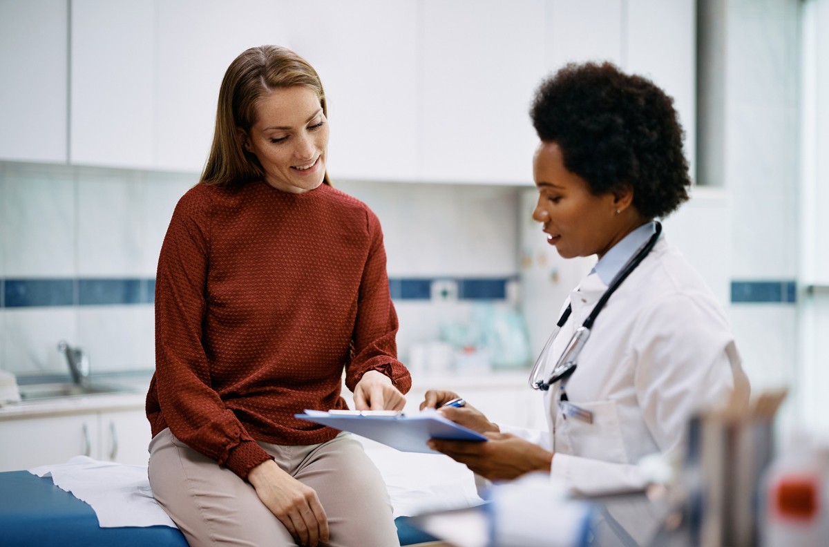 African American doctor and her female patient analyzing medical report after examination in the hospital. Focus is on female patient.