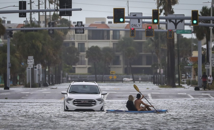 30.08.2023, USA, St. Pete Beach: Ein Mann und eine Frau fahren mit dem Kajak an einem verlassenen Fahrzeug an der Kreuzung von Boca Ciega Drive und Pasadena Avenue vorbei. Hurrikan «Idalia» ist an der ...