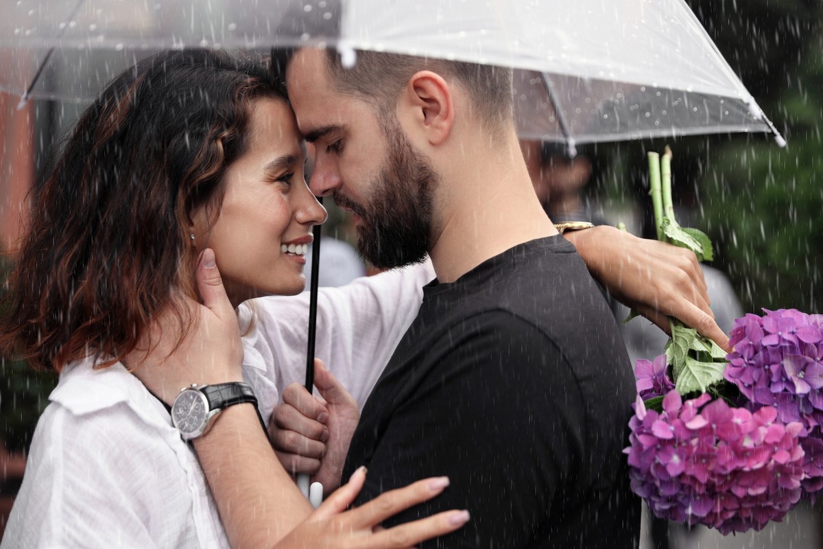 Young couple with umbrella enjoying time together under rain on city street