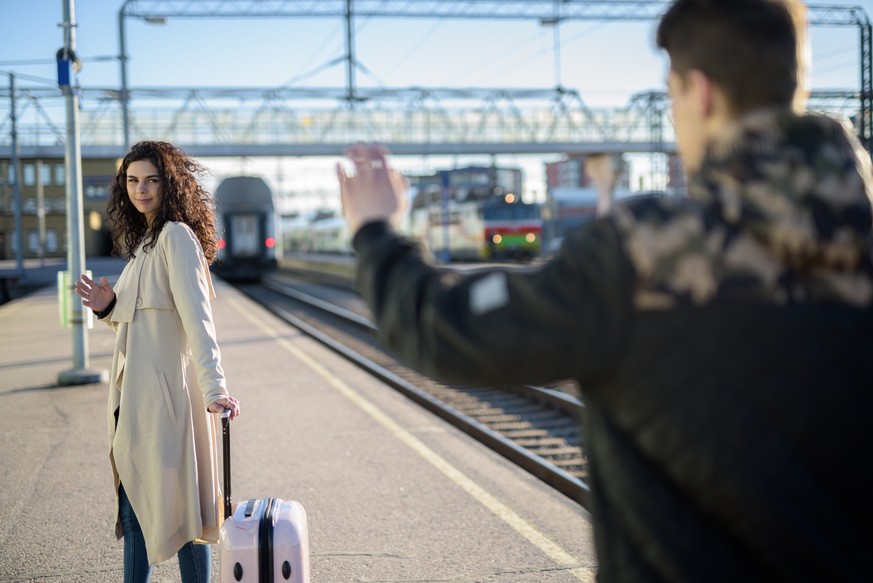 Separation of young couple woman leaving with suitcase at train station platform while boyfriend waving horizontal shot