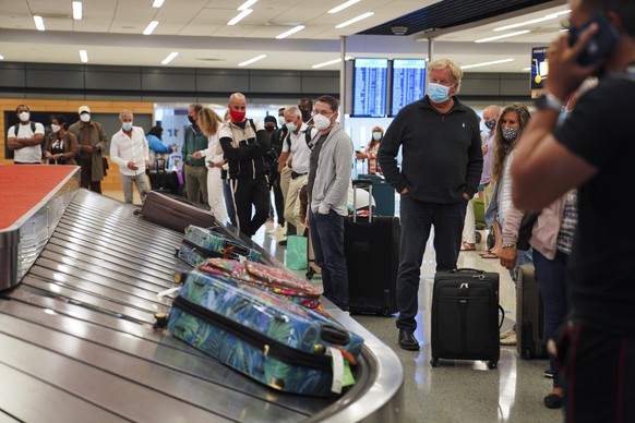 Dicht an dicht warten Passagiere an einem Flughafen auf ihre Koffer. Eine Maske wird getragen, der Abstand nicht immer eingehalten.