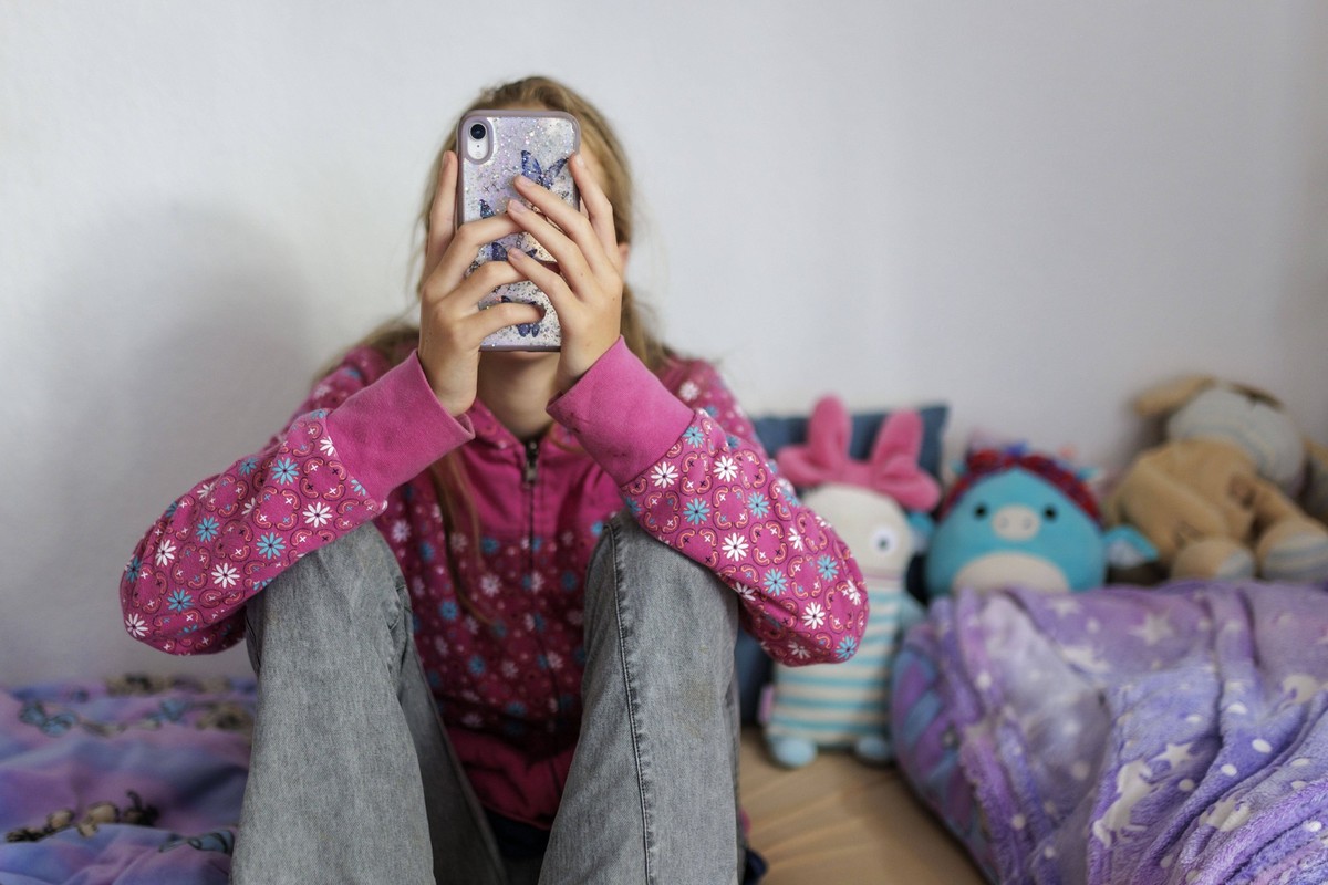 Symbolfoto zum Thema Handynutzung bei Kindern: Ein Maedchen sitzt in ihrem Bett und ist am Handy. Berlin, 22.07.2025. Berlin Deutschland *** Symbolic photo on the topic of cell phone use by children A ...