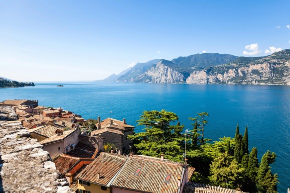 Ein Symbolfoto von Malcesine am Gardasee. Hier der Blick aus dem Castello Scaligero auf den See bei bestem Wetter. Am Ufer des Gardasees in der Stadt Malcesine. Grüne Bäume und blaues Wasser.