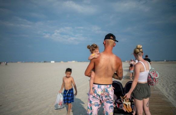 WILDWOOD, NJ - JULY 03: A father with a sunburned back carries his daughter on July 3, 2020 in Wildwood, New Jersey. New Jersey beaches have reopened for the July 4th holiday as some coronavirus restr ...