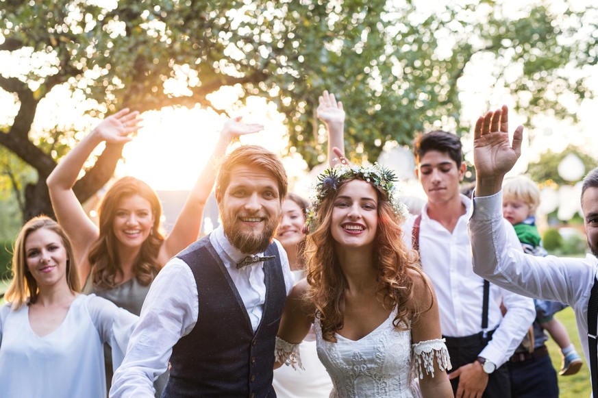 Wedding reception outside in the backyard. Family celebration. Bride, groom and their guests posing for the photo at sunset.