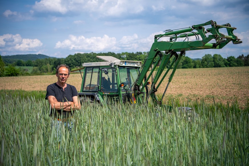 PRODUKTION - 18.05.2022, Nordrhein-Westfalen, Detmold: Ulf Allhoff-Cramer, Landwirt, steht in einem Roggen-Feld vor seinem Traktor. Der Bio-Bauer macht den Autokonzern VW mitverantwortlich f
