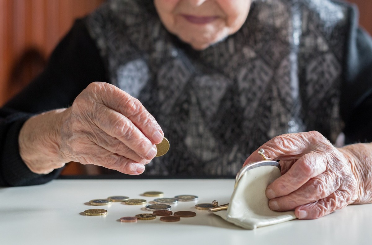 Elderly 95 years old woman sitting miserably at the table at home and counting remaining coins from the pension in her wallet after paying the bills.