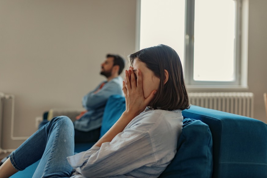 Unhappy Couple After an Argument in the Living Room at Home. Sad Pensive Young Girl Thinking of Relationships Problems Sitting on Sofa With Offended Boyfriend, Conflicts in Marriage, Upset Couple Afte ...