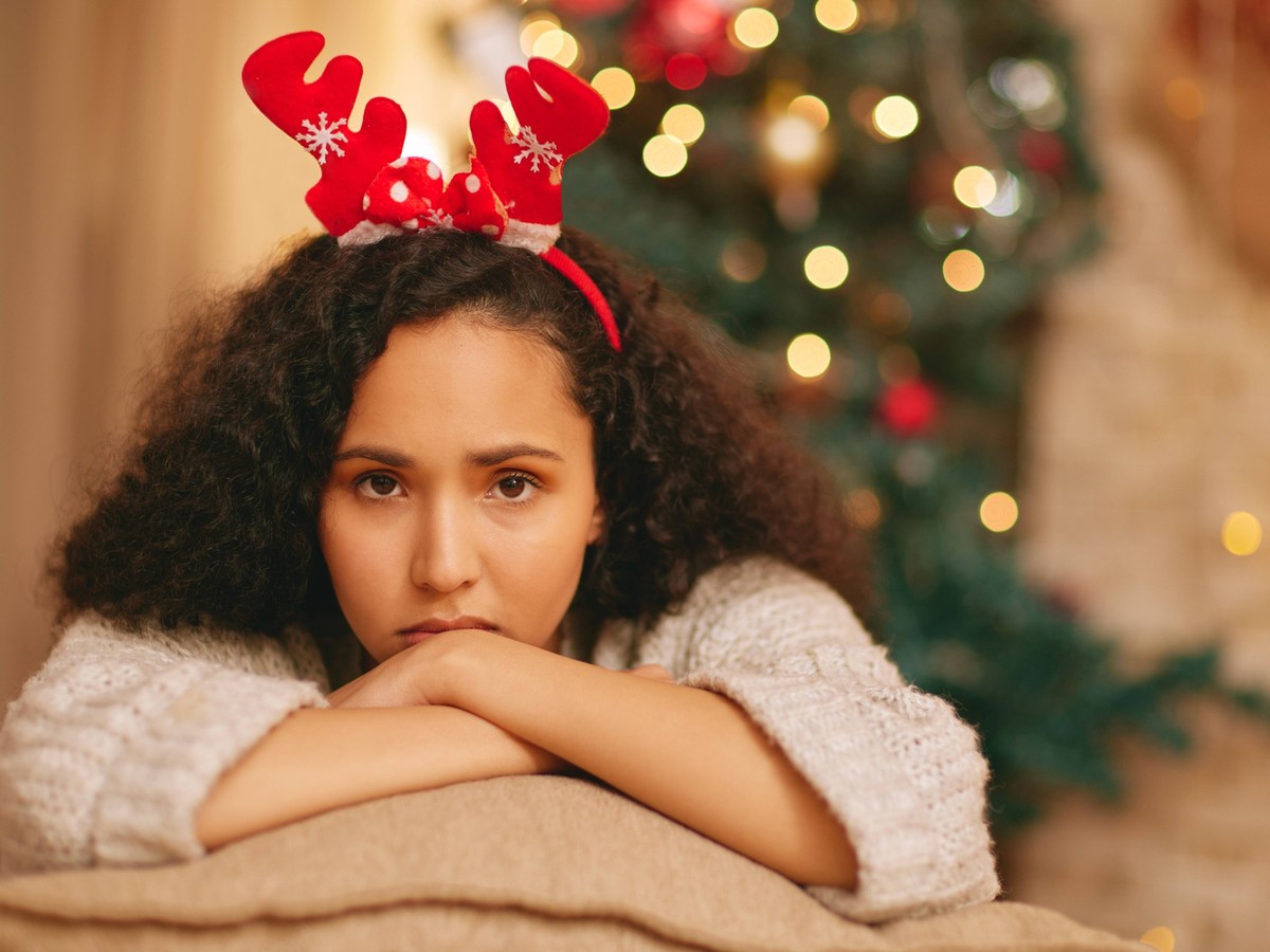 Portrait, lonely and sad woman on sofa at Christmas with crisis, frustrated face and holiday in lounge at home. Mental health, vacation and girl with depression on couch in living room with xmas tree  ...